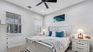 A bedroom with a bed, nightstands, a ceiling fan, and a window with blinds. - Naples Luxury Cottage-Stylish 2BR in Premier Luxury Community (Naples)
