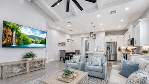 A spacious living room with a large TV, a dining area, a kitchen, and a view of a waterfall. - Naples Luxury Cottage-Stylish 2BR in Premier Luxury Community (Naples)