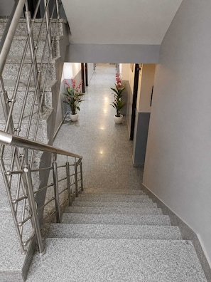 A staircase with metal railings leading to a landing, a hallway with a polished floor, and potted plants. - Hotel Popular Suites (New Delhi)