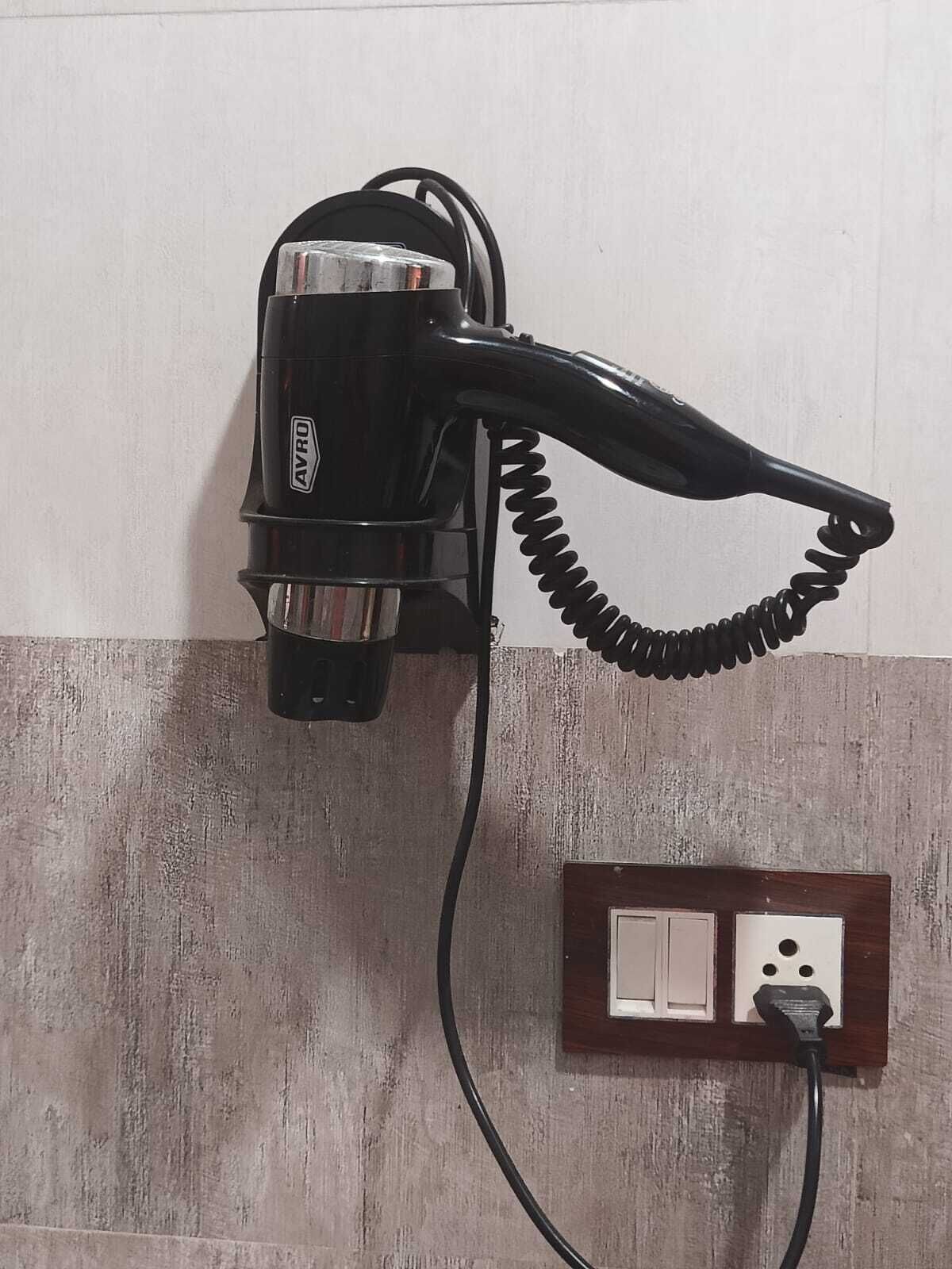 A hair dryer mounted on a wall with a power outlet below it.