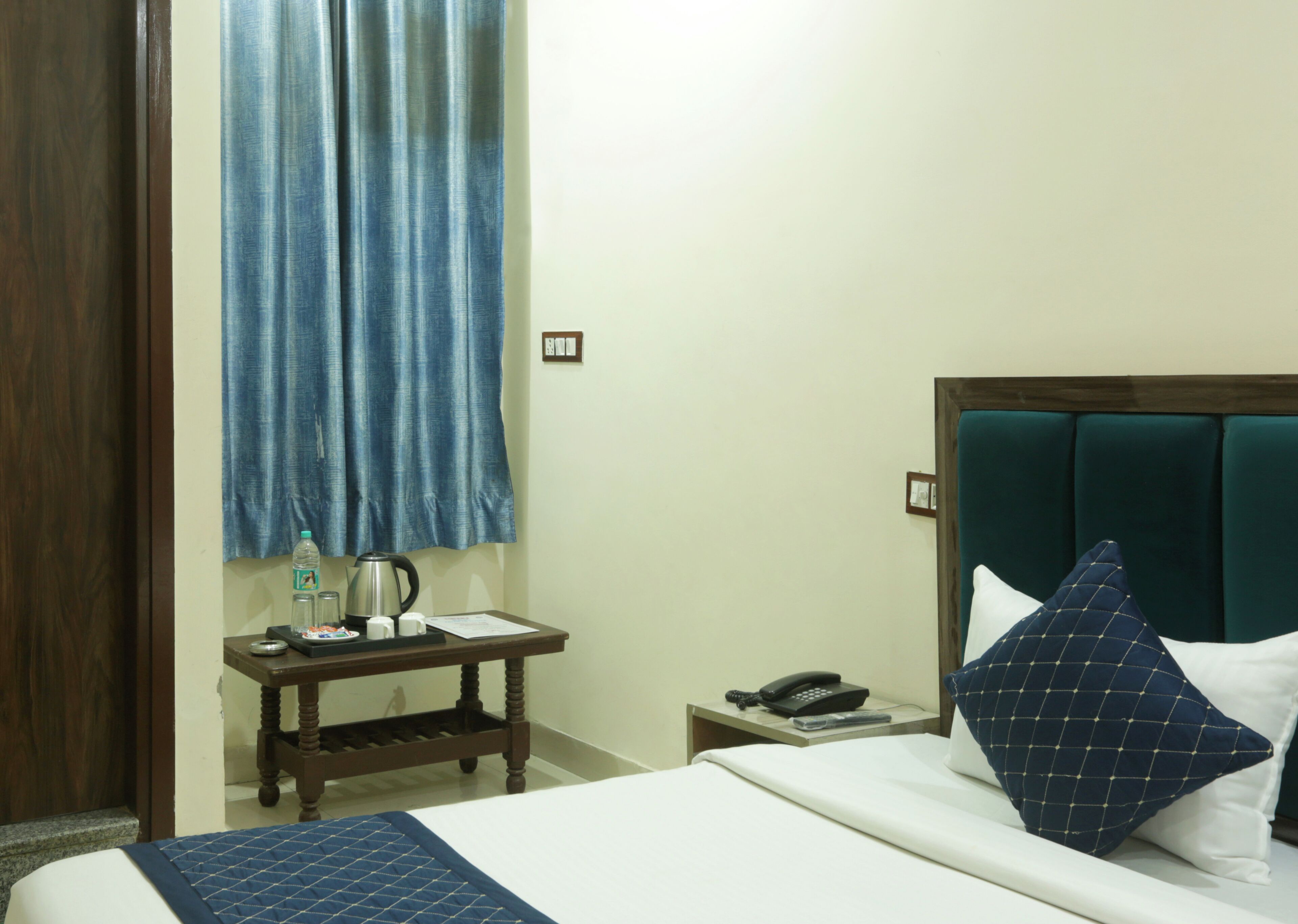 A hotel room with a bed, a bedside table with a kettle, a phone, and a water bottle.