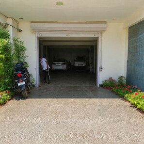 En garageindgang med en person stående indenfor, to parkerede biler og en motorcykel udenfor.