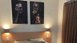 A bedroom with a bed, two wall-mounted lamps, a nightstand with books, and two framed artworks on the wall. - Great value for money in Chapada! (Seabra)