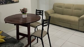 A living room with a beige sofa, a round wooden dining table with two chairs, a potted plant, and two wall-mounted paintings. - Great value for money in Chapada! (Seabra)