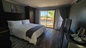 A bedroom with a bed, a desk with a chair, a television, and a balcony with a view. - Zebra Hilltop Lodge (Mazunga)