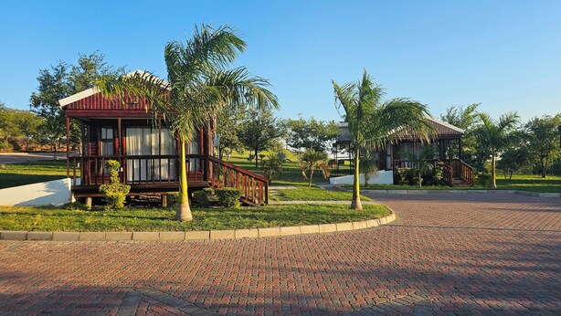 A wooden structure with a balcony, surrounded by palm trees and a brick pathway. - Zebra Hilltop Lodge (Mazunga)