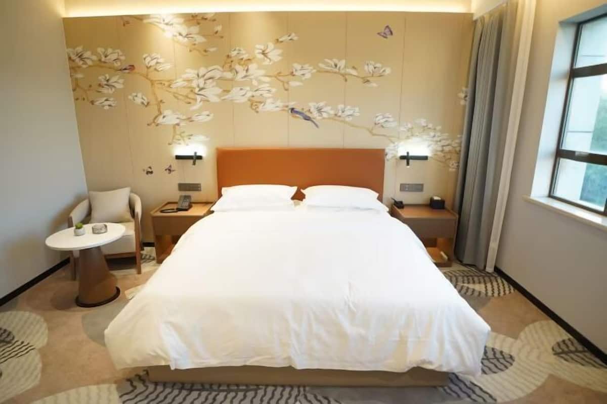 A hotel room with a bed, nightstands, a chair, a small table, and a wall with floral wallpaper.