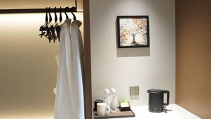 Habitación de hotel con una toalla blanca colgada en un perchero, un cuadro enmarco de un árbol, una bandeja con una cafetera, una taza y botellas de agua.
