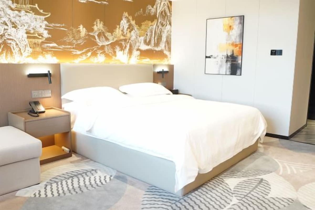 Quarto de hotel com uma cama grande, mesas de cabeceira, abajur e um quadro na parede.