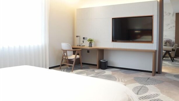 Una habitación de hotel moderna con cama, escritorio, silla, ventana grande y espejo.