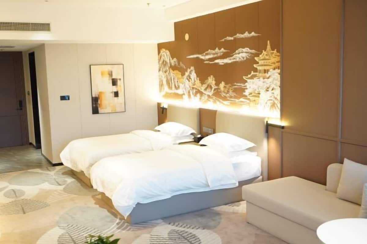 A hotel room with a bed, a sofa, a wall with a decorative mural, and a patterned carpet.
