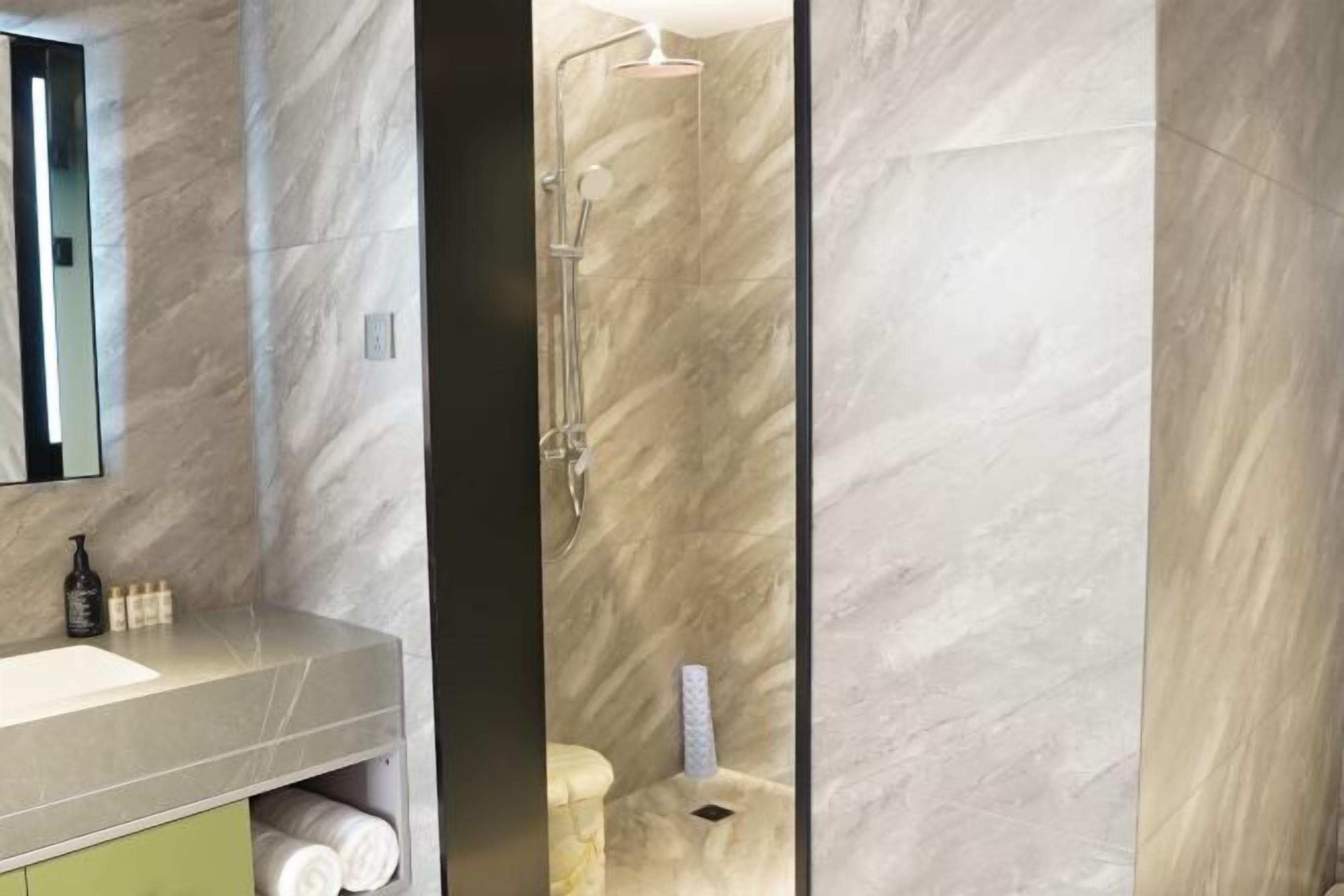 A bathroom with a marble sink, a mirror, a shower with a glass door, and towels stored in a cabinet.