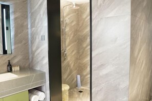Un baño con lavamanos de mármol, un espejo, ducha con puerta de cristal y toallas guardadas en un armario.