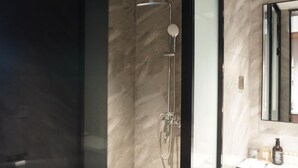 Un baño moderno con cabina de ducha de vidrio, pared de mármol y espejo con marco negro.