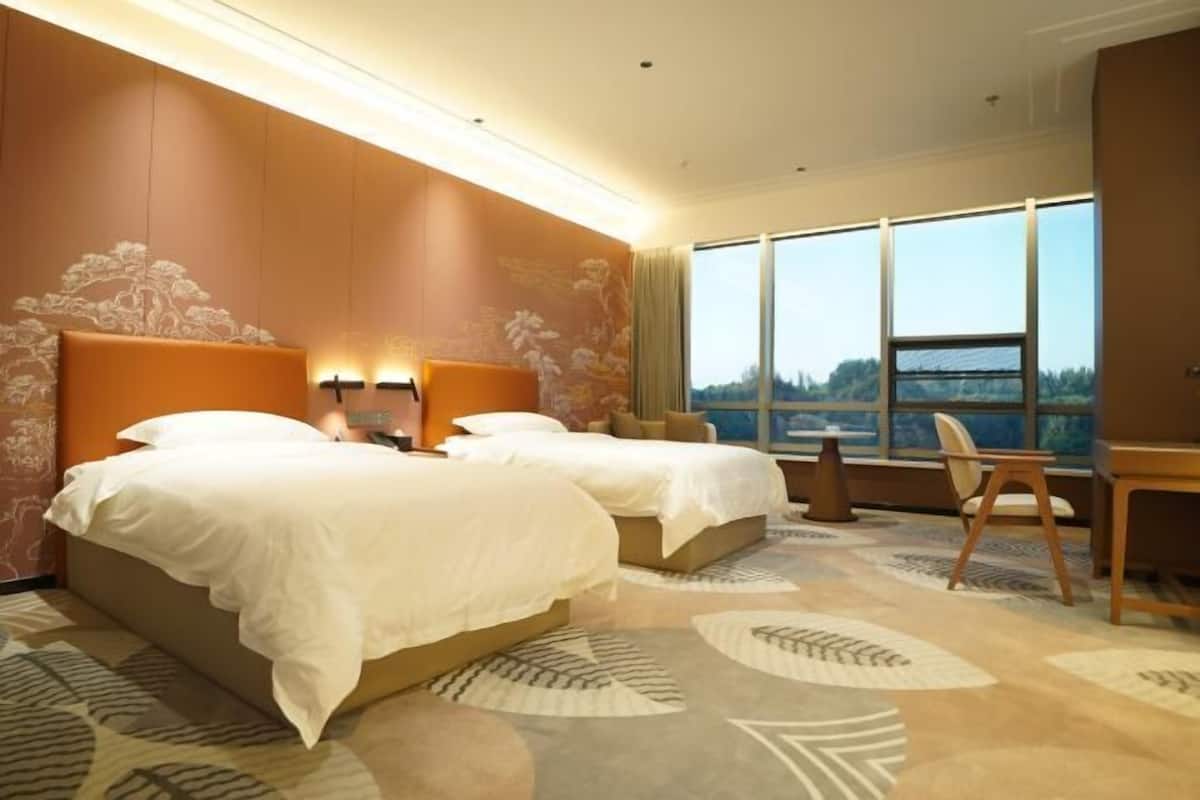 A hotel room with two beds, a desk, and a view of the outdoors.