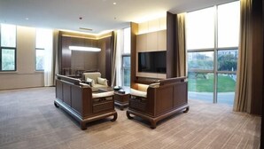 Una habitación de hotel espaciosa con un gran ventanal, un televisor de pantalla plana y una zona de estar con sofá y sillones.