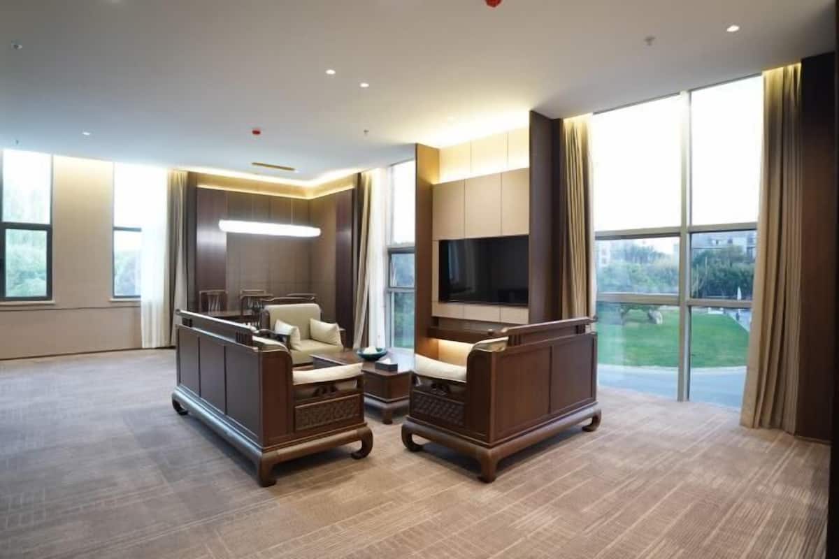 A spacious hotel room with a large window, a flat-screen TV, and a seating area with a sofa and armchairs.