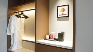 Habitación de hotel con cama, mesita de noche con artículos de aseo, un cuadro en la pared y un perchero.