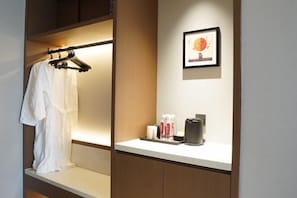 Habitación de hotel con cama, mesita de noche con artículos de aseo, un cuadro en la pared y un perchero.
