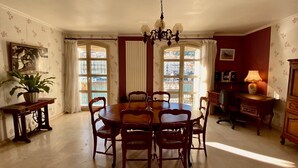A dining room with a round table, chairs, a chandelier, and a view through large windows.