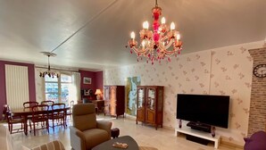 A living room with a chandelier, a television, a sofa, a dining area, and a map on the wall.