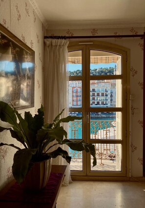Een kamer met een groot raam, een potplant en een lijst met een afbeelding aan de muur.