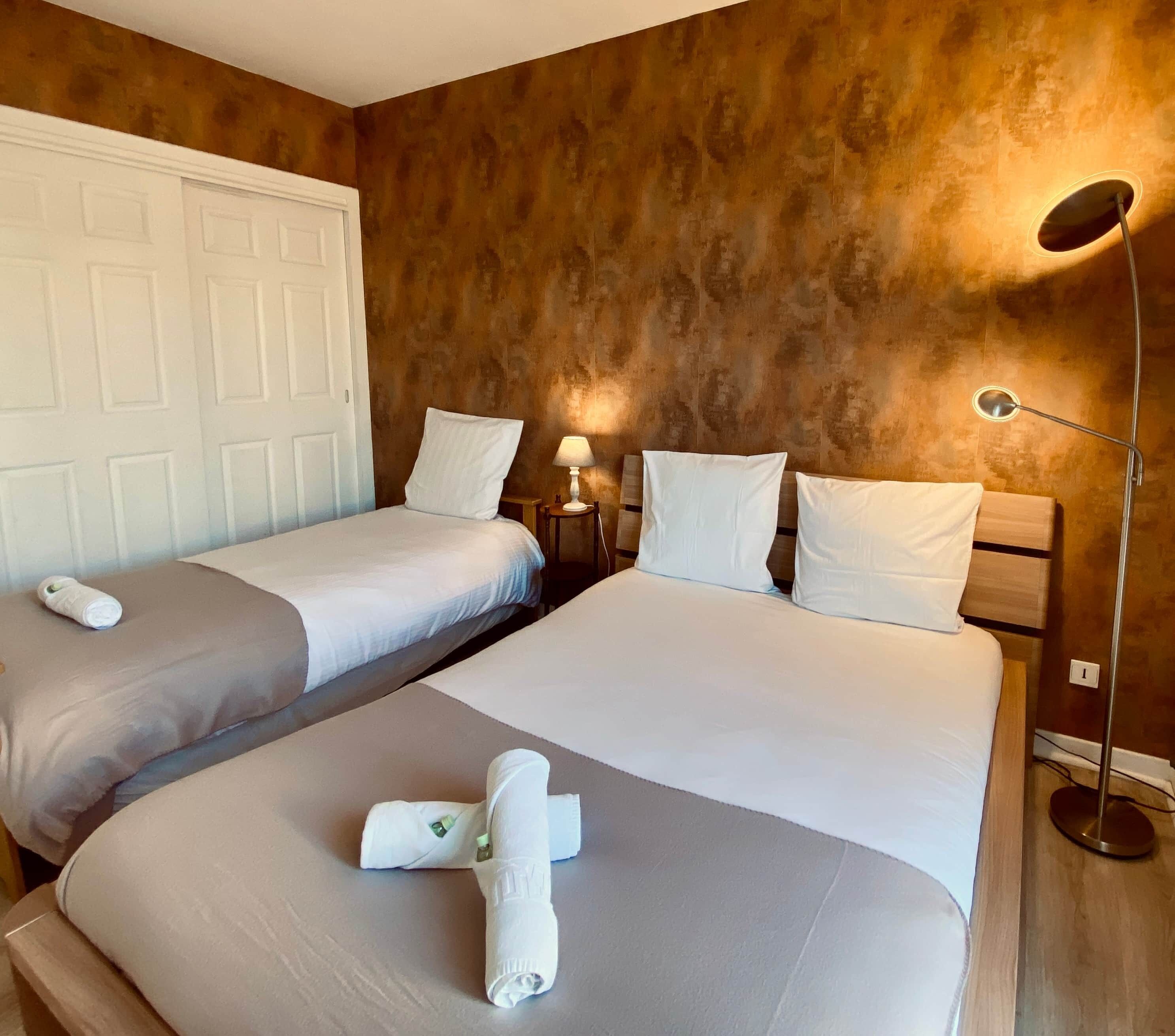 A hotel room with two beds, a door, a lamp, and a wall with a textured finish.