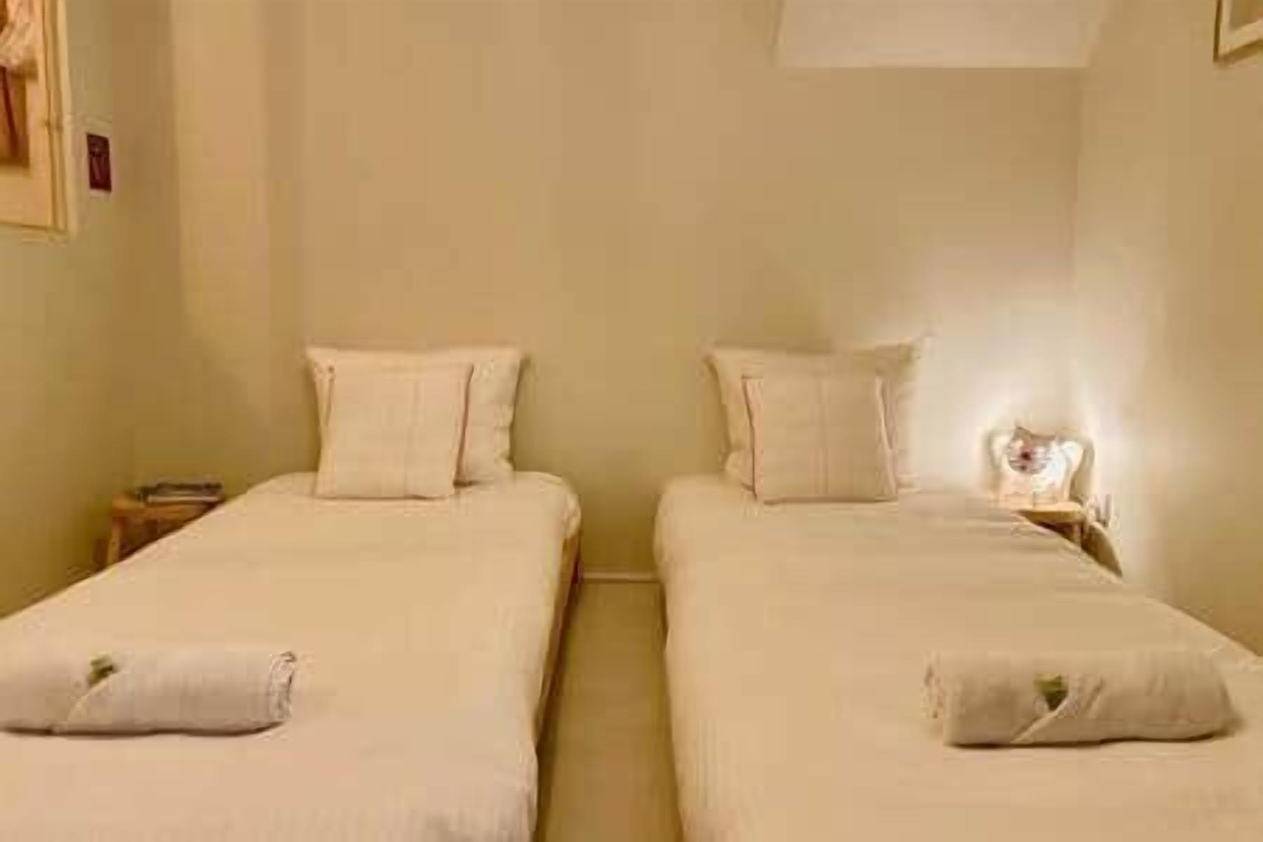 Two single beds with pillows, a nightstand, and a wall-mounted light.
