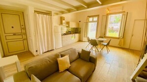 A living room with a sofa, a dining table with chairs, a kitchen area, and a staircase. - "Suzon" Cosy little loft with terrace (Sète)