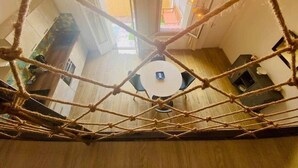 A high ceiling with a rope net, a round table, and a view of a wooden floor and a window. - "Suzon" Cosy little loft with terrace (Sète)