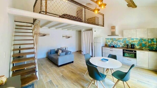 A loft-style room with a staircase, a sofa, a dining table with chairs, and a kitchen area. - "Suzon" Cosy little loft with terrace (Sète)