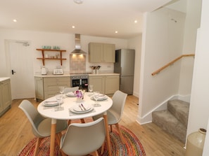 A compact kitchen with modern appliances, a dining table set for four, and a staircase leading to an upper level. - Dairy Cottage (Kirkby Stephen)