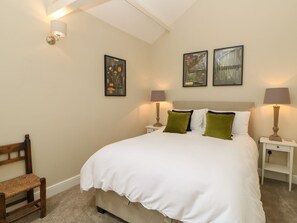 A neatly made bed with white bedding, two green pillows, a wooden chair, and two bedside tables with lamps. - Dairy Cottage (Kirkby Stephen)
