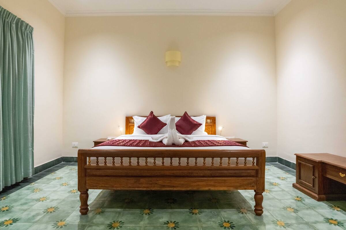 Cama de casal com estrutura de madeira, duas almofadas vermelhas e um cobertor vermelho.