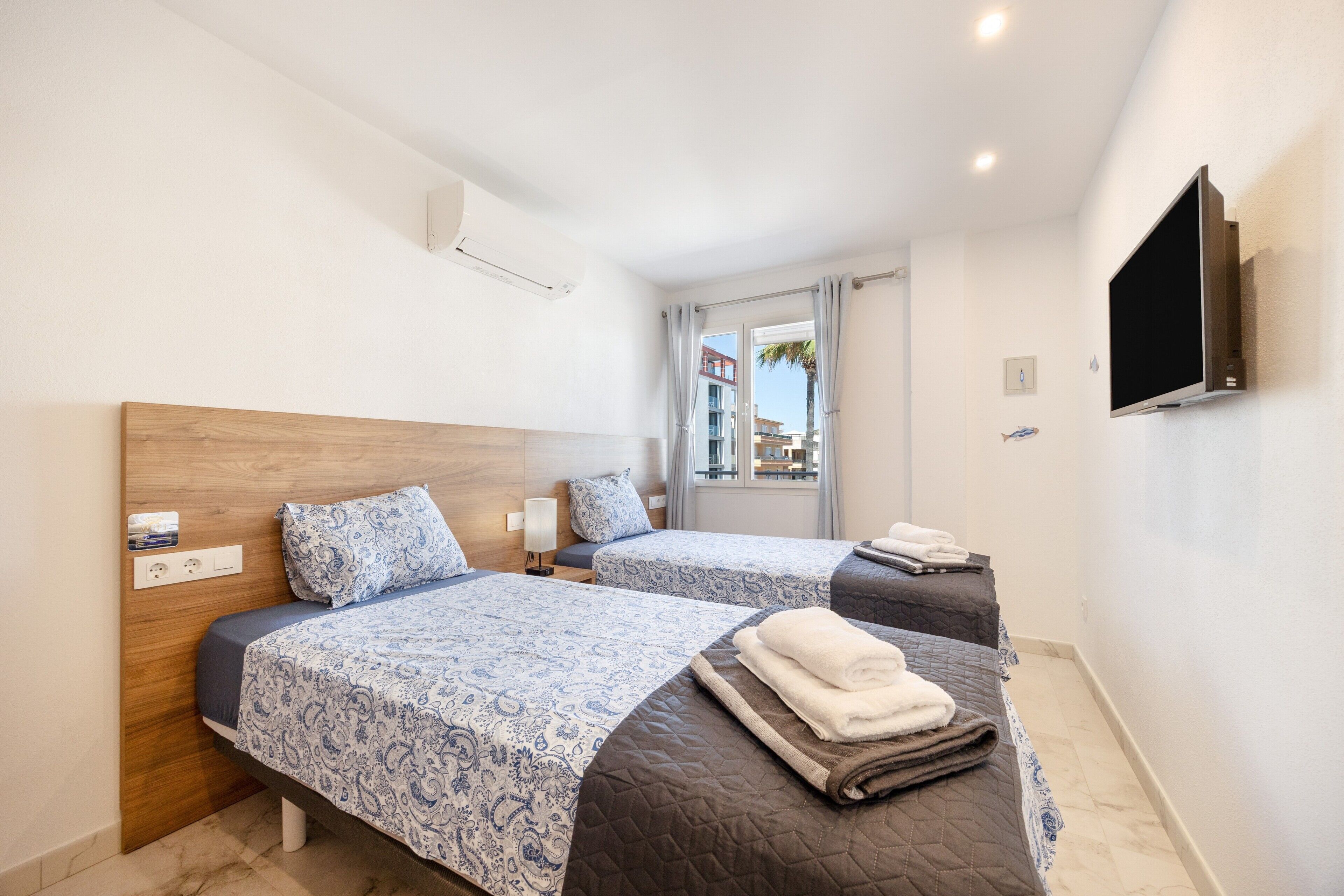 Una camera d'albergo con due letti, una TV montata a parete e una finestra con tende.