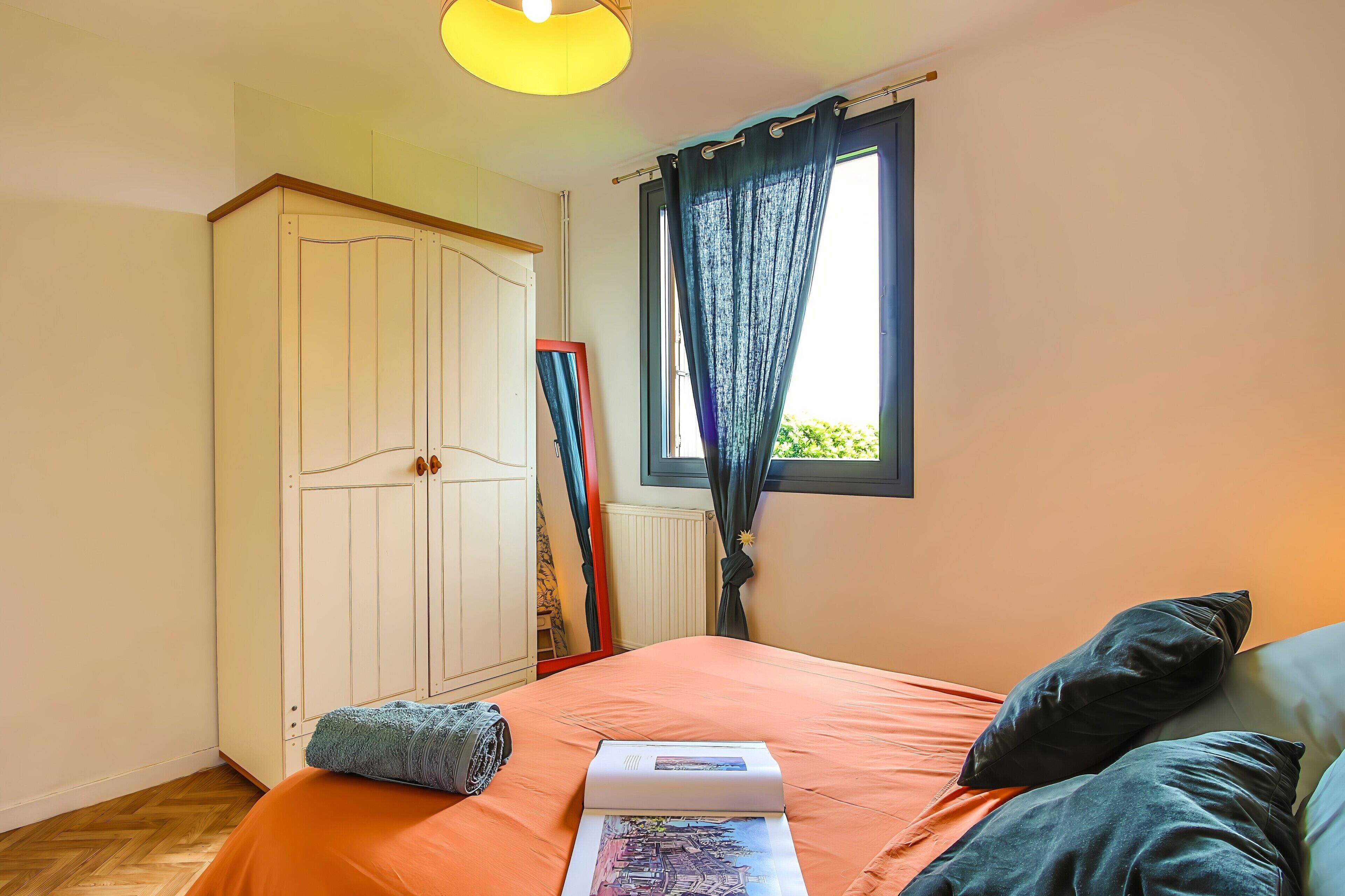 Un dormitorio con cama, armario, ventana con cortinas y radiador.