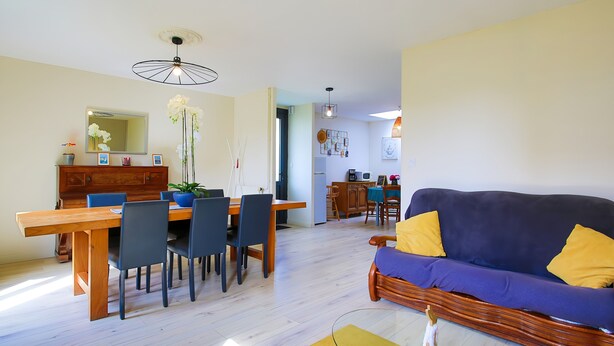 A dining area with a wooden table and chairs, a sofa with yellow cushions, and a mirror above the table. - Holiday Home 'Gite De Pauline, Sainte-mère-église' with Private Terrace, Private Garden and Wi-Fi (Sainte-Mère-Église)