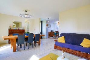 A dining area with a wooden table and chairs, a sofa with yellow cushions, and a mirror above the table. - Holiday Home 'Gite De Pauline, Sainte-mère-église' with Private Terrace, Private Garden and Wi-Fi (Sainte-Mère-Église)