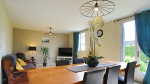 A dining area with a wooden table, chairs, a TV, and a plant. - Holiday Home 'Gite De Pauline, Sainte-mère-église' with Private Terrace, Private Garden and Wi-Fi (Sainte-Mère-Église)