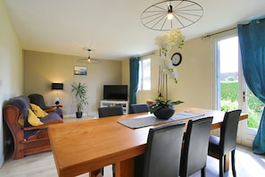 A dining area with a wooden table, chairs, a TV, and a plant. - Holiday Home 'Gite De Pauline, Sainte-mère-église' with Private Terrace, Private Garden and Wi-Fi (Sainte-Mère-Église)
