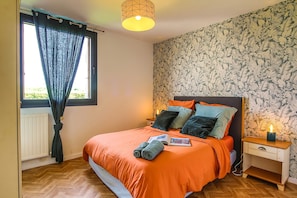 Een slaapkamer met een bed, een nachtkastje, een raam met gordijnen en een muur met een bladpatroon.