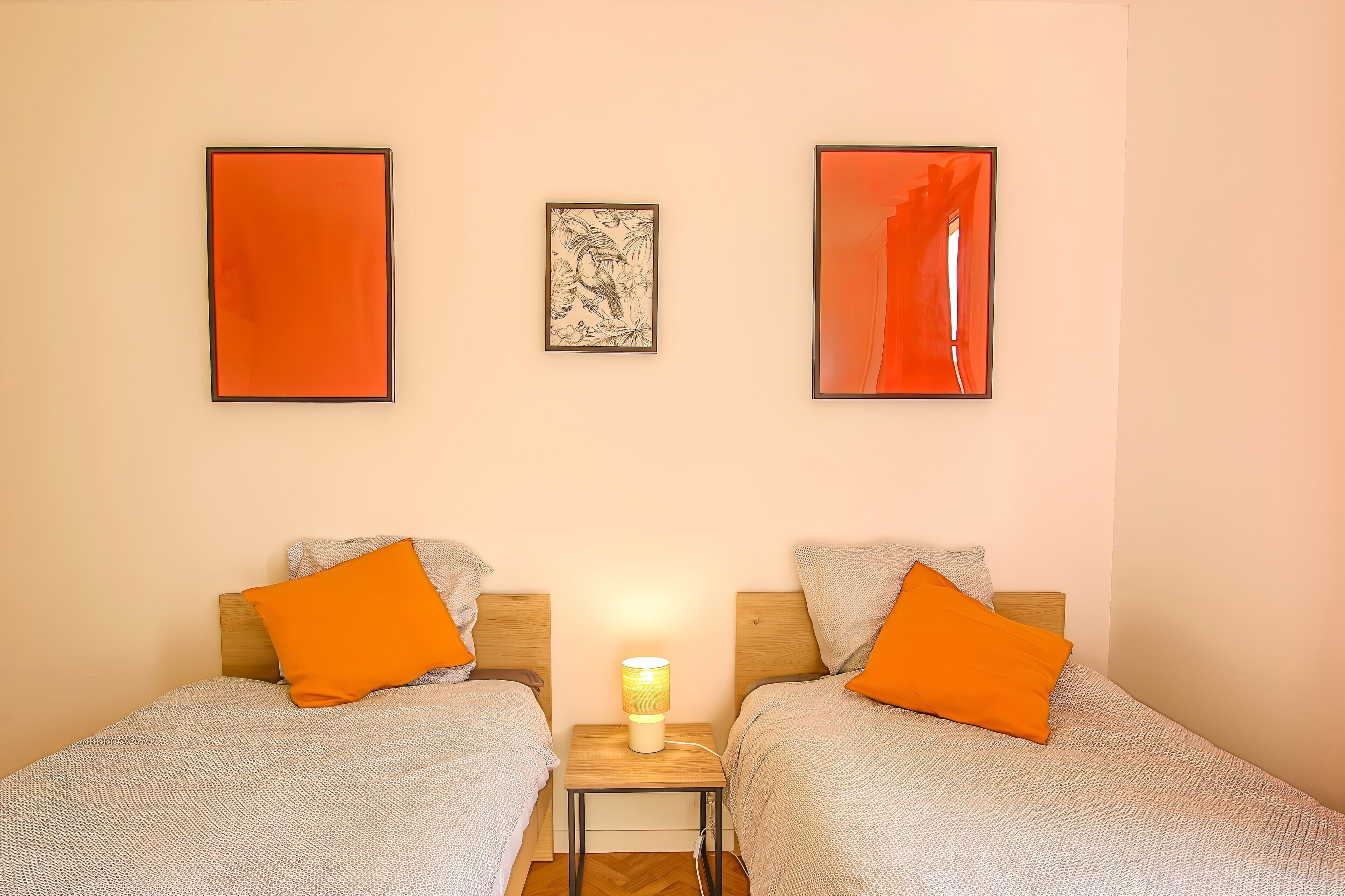 A room with two beds, a nightstand with a lamp, and three framed pictures on the wall.