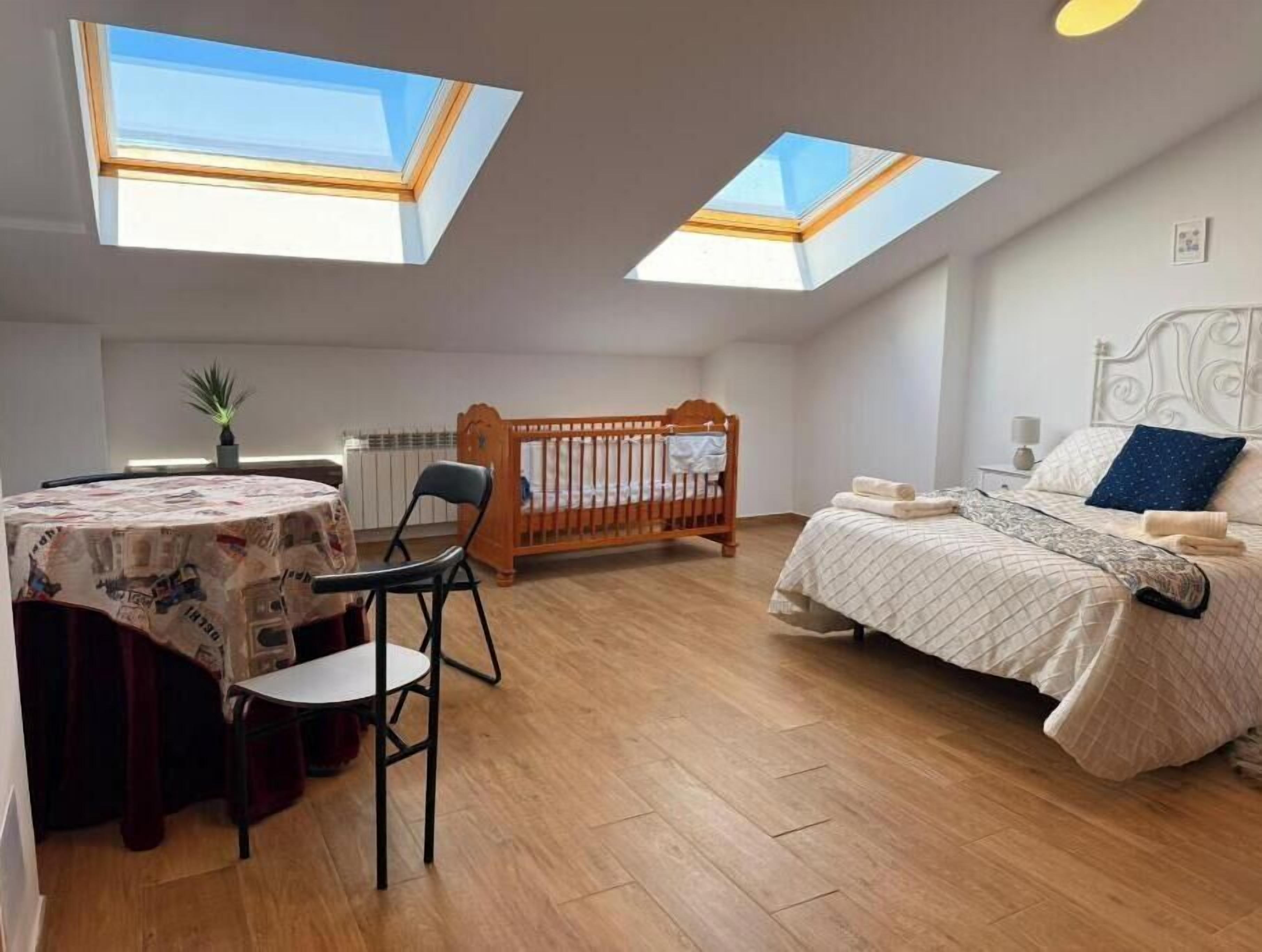 Un dormitorio con cama, cuna, mesa y silla, y tragaluces.