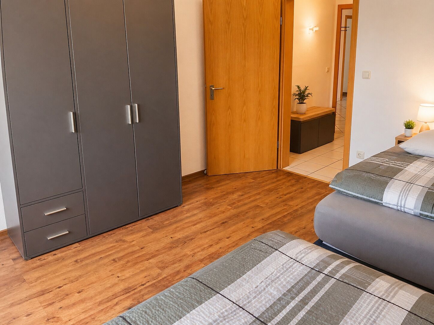 Une chambre à coucher avec un lit, une armoire, un plancher en bois et une table de chevet avec une lampe.