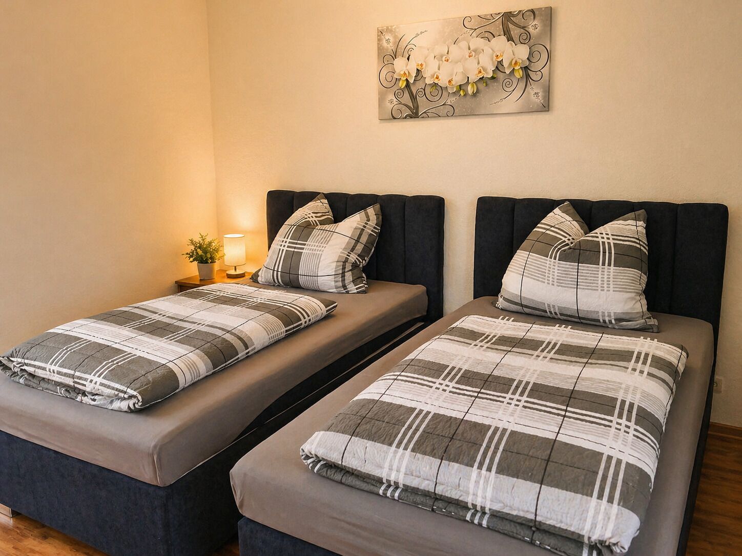 Twee eenpersoonsbedden met bijpassend beddengoed, een nachtkastje met een lamp en een aan de muur hangend kunstwerk.