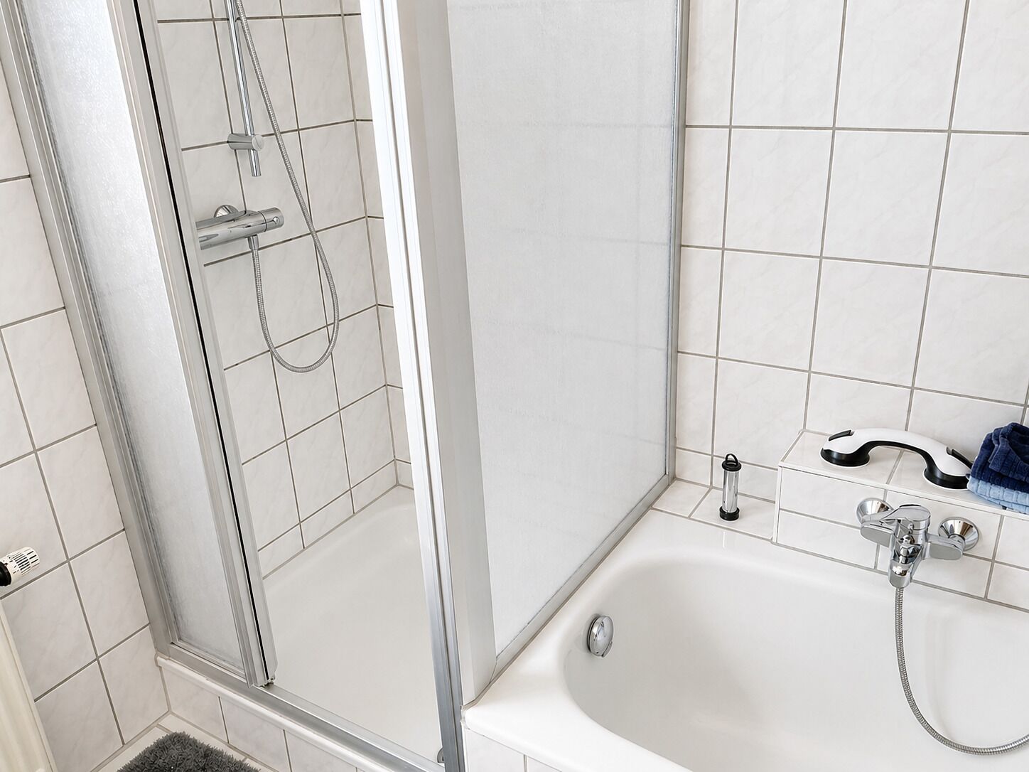 A bathroom with a glass shower enclosure, a bathtub, and a white tiled wall.
