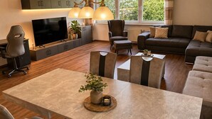 Un salon moderne comprenant un téléviseur, un canapé, une table à manger, des chaises et une grande fenêtre.