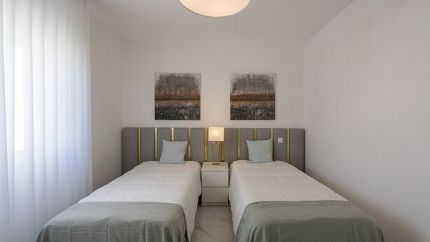 Habitación de hotel con dos camas, una mesita de noche, una lámpara y dos cuadros colgados en la pared.