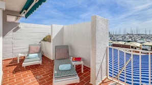 Un balcon avec deux fauteuils de jardin à rayures, une petite table avec des livres et une vue sur une marina remplie de bateaux.