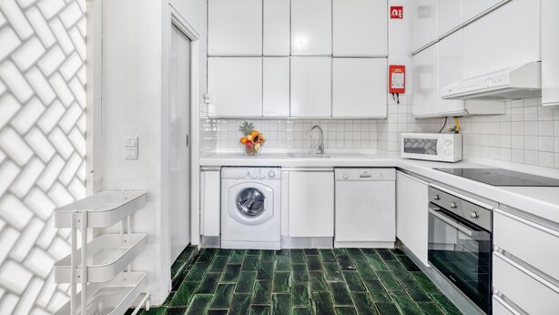 Une cuisine compacte avec des meubles blancs, un lave-linge, un four à micro-ondes et un sol carrelé.